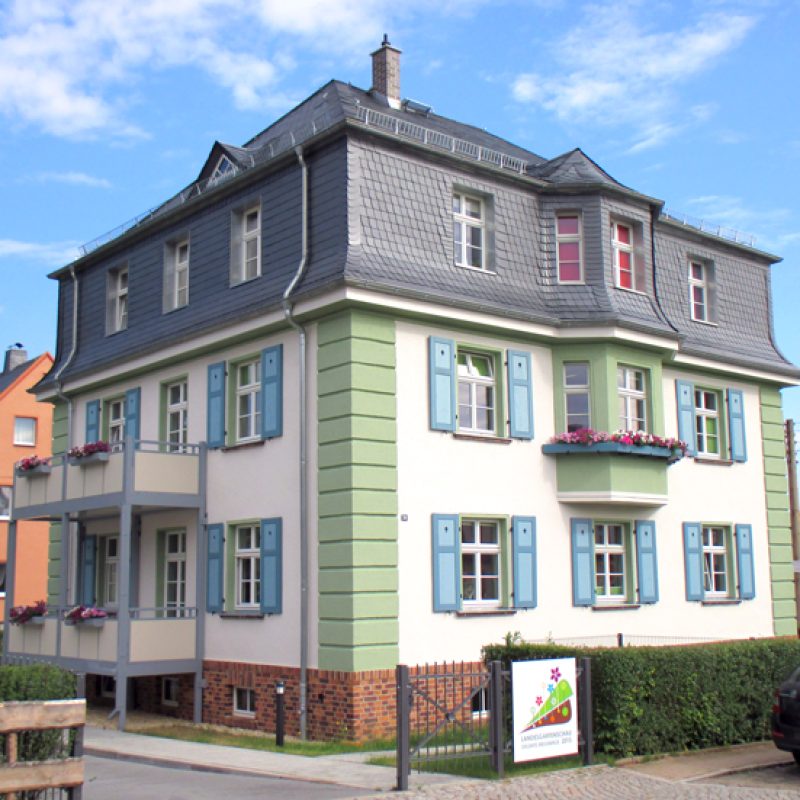 Stadtvilla mit grün-weißer Fassade und blauen Fensterläden