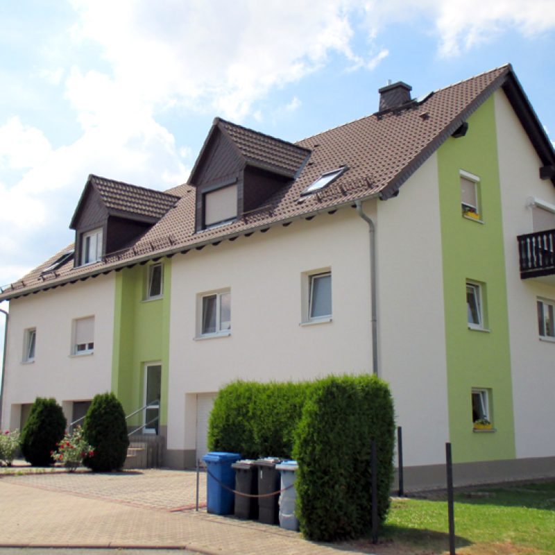 Mehrfamilienhaus mit weißer Fassade und hellgrünen Akzentflächen