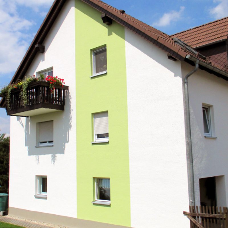 Wohnhaus mit weißer Fassade und hellgrünem Farbstreifen