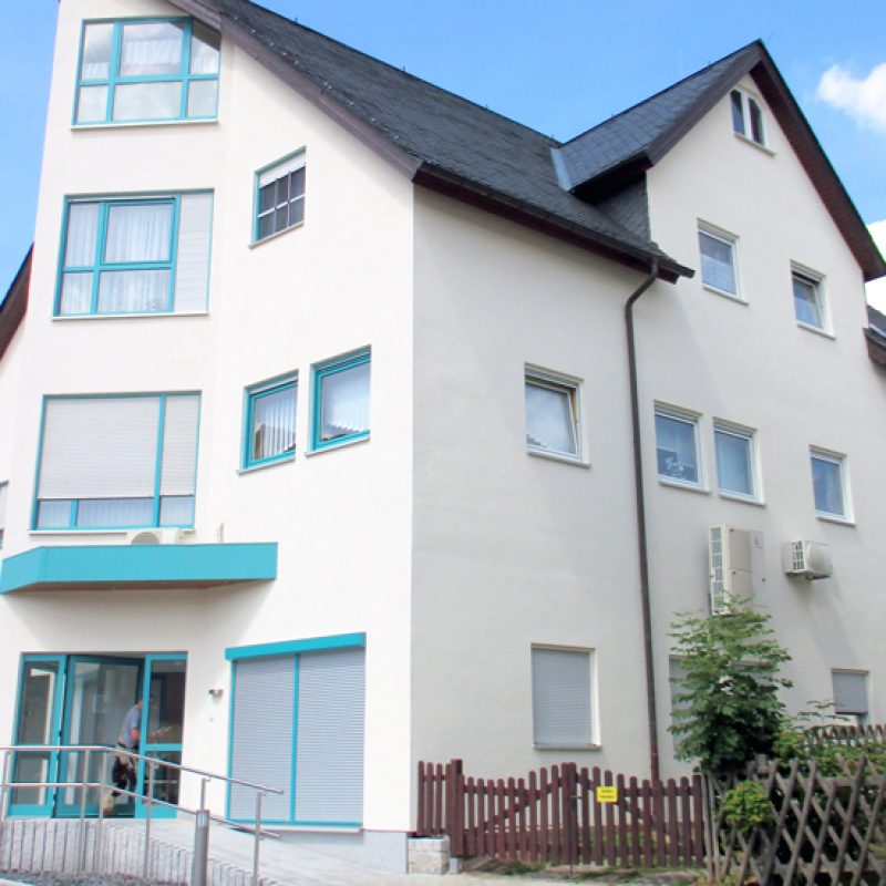 Wohn- und Geschäftshaus mit weißer Fassade und türkisfarbenen Fensterrahmen