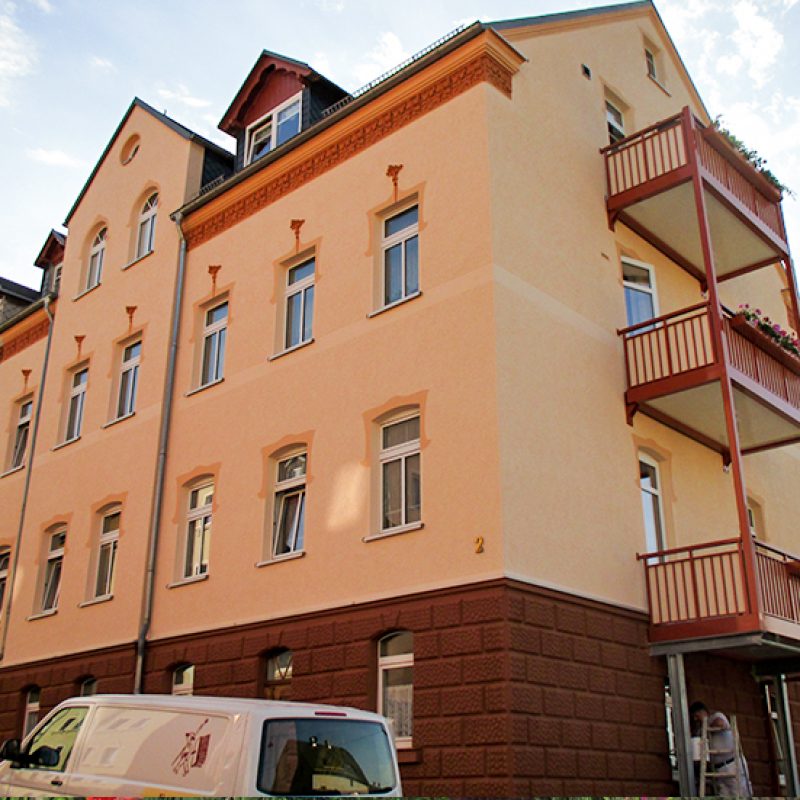 Mehrfamilienhaus mit apricotfarbener Fassade und roten Balkonen