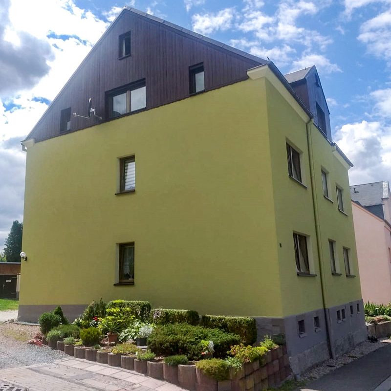 Mehrfamilienhaus mit gelbgrüner Fassade und dunkler Verkleidung im Dachgeschoss