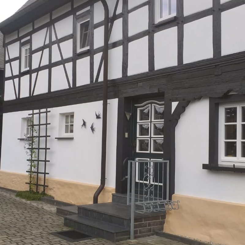 Fachwerkhaus mit weißen Gefachen und dunklem Holzwerk, Eingangsseite