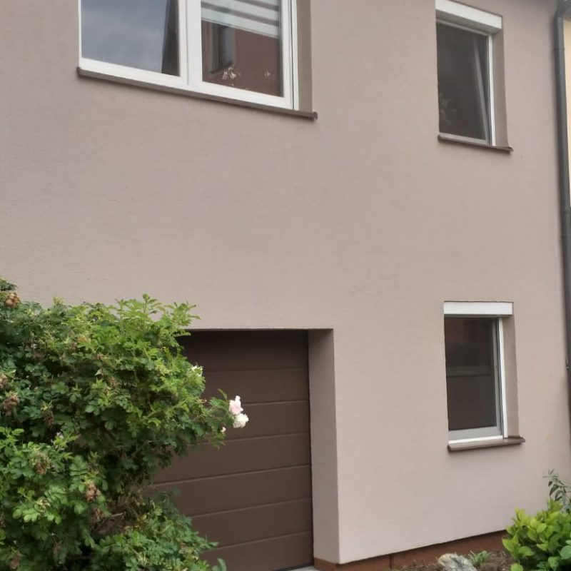 Wohnhaus mit hellgrau-beiger Fassade und Garagentor